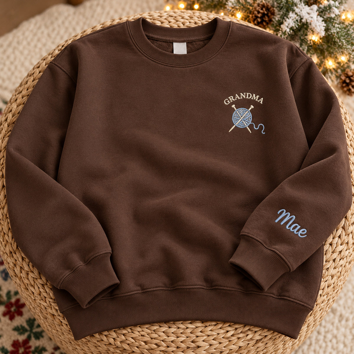 Grandma's Knitting sweatshirt concept mockup featuring a ball of yarn and crossed knitting needles, sample personalization Mae, hero view