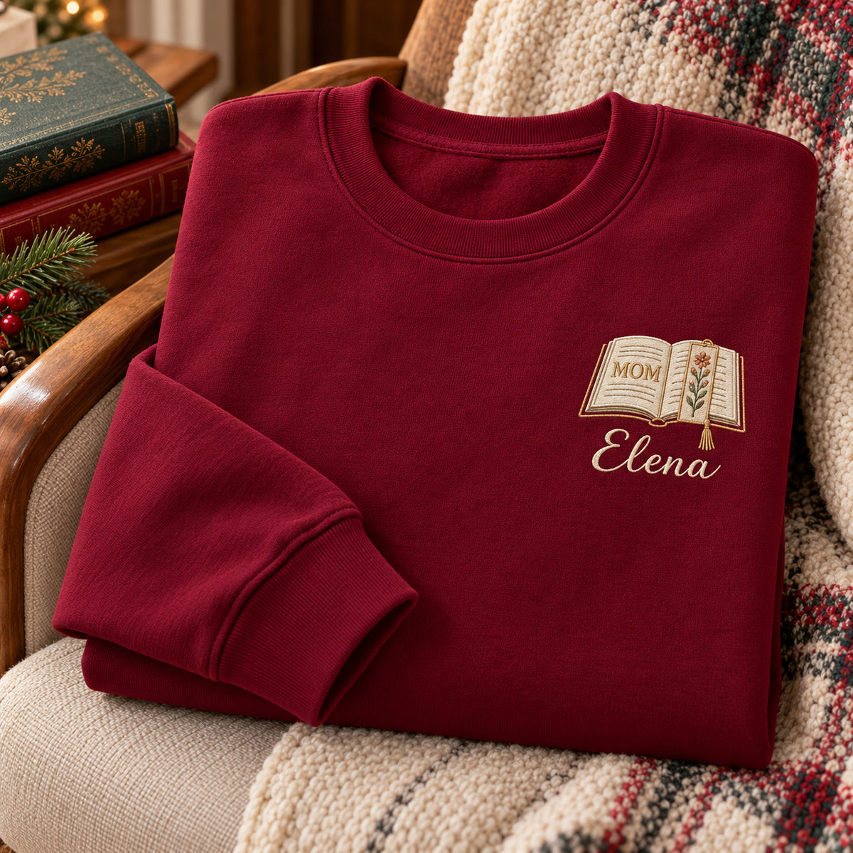 Motherhood Chapter sweatshirt concept mockup featuring an open book with a floral page and bookmark, sample personalization Elena, hero view