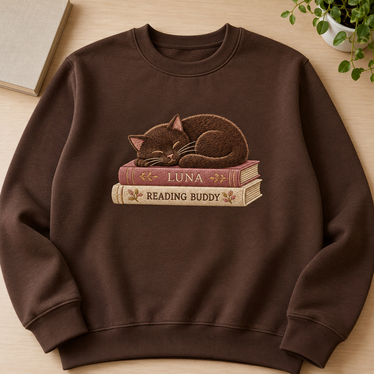 Reading Buddy Cat sweatshirt concept mockup featuring a sleeping cat curled on two books, sample personalization LUNA, hero view