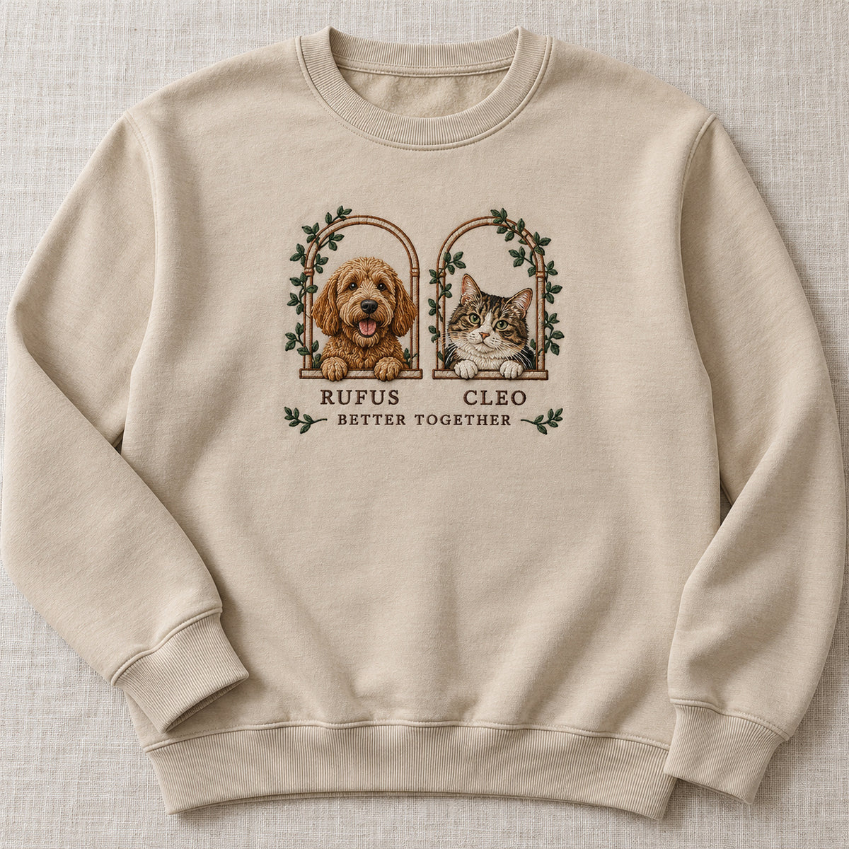 Two Little Windows sweatshirt concept mockup featuring a dog and cat in two leafy arched windows, sample personalization RUFUS CLEO, hero view