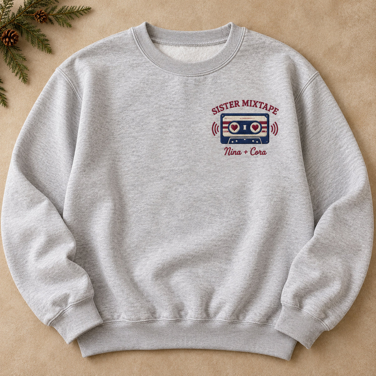 Sister Mixtape sweatshirt concept mockup featuring a cassette tape with heart-shaped reel centers, sample personalization Nina + Cora, hero view