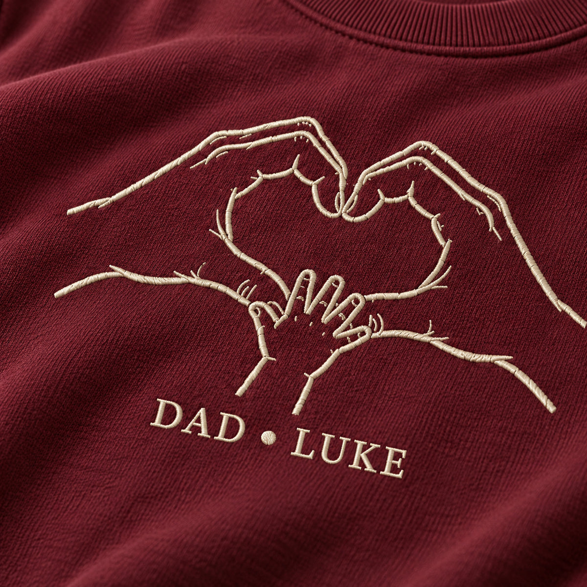 Heart In Our Hands personalized Dad hands design; Maroon sweatshirt mockup, embroidery detail; sample text DAD • LUKE