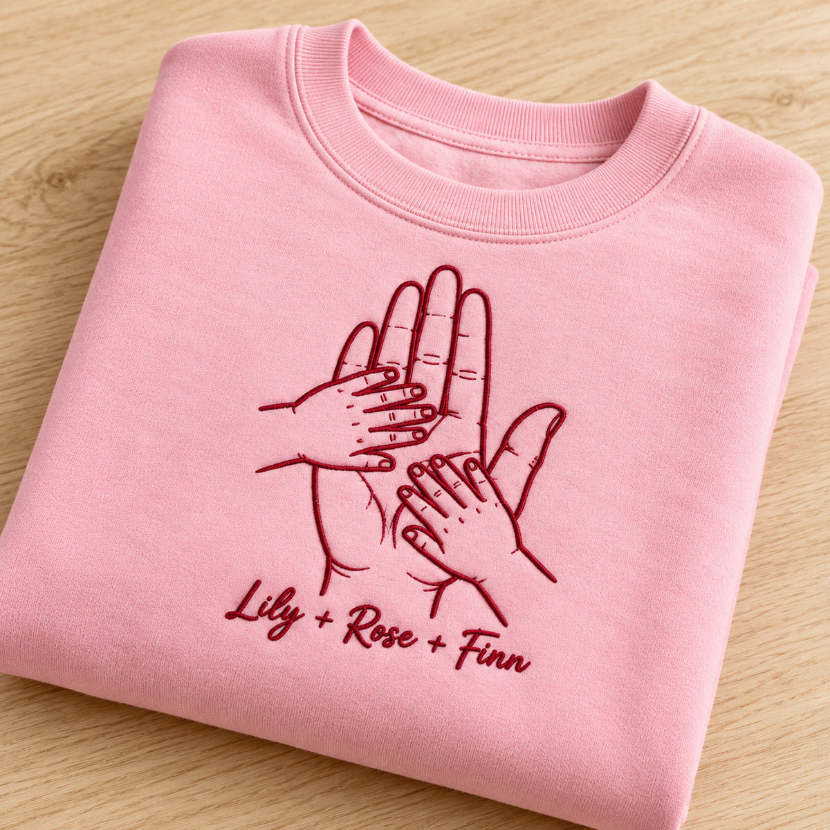 Held by Love personalized Family hands design; Light Pink sweatshirt mockup, personalization detail; sample text Lily + Rose + Finn