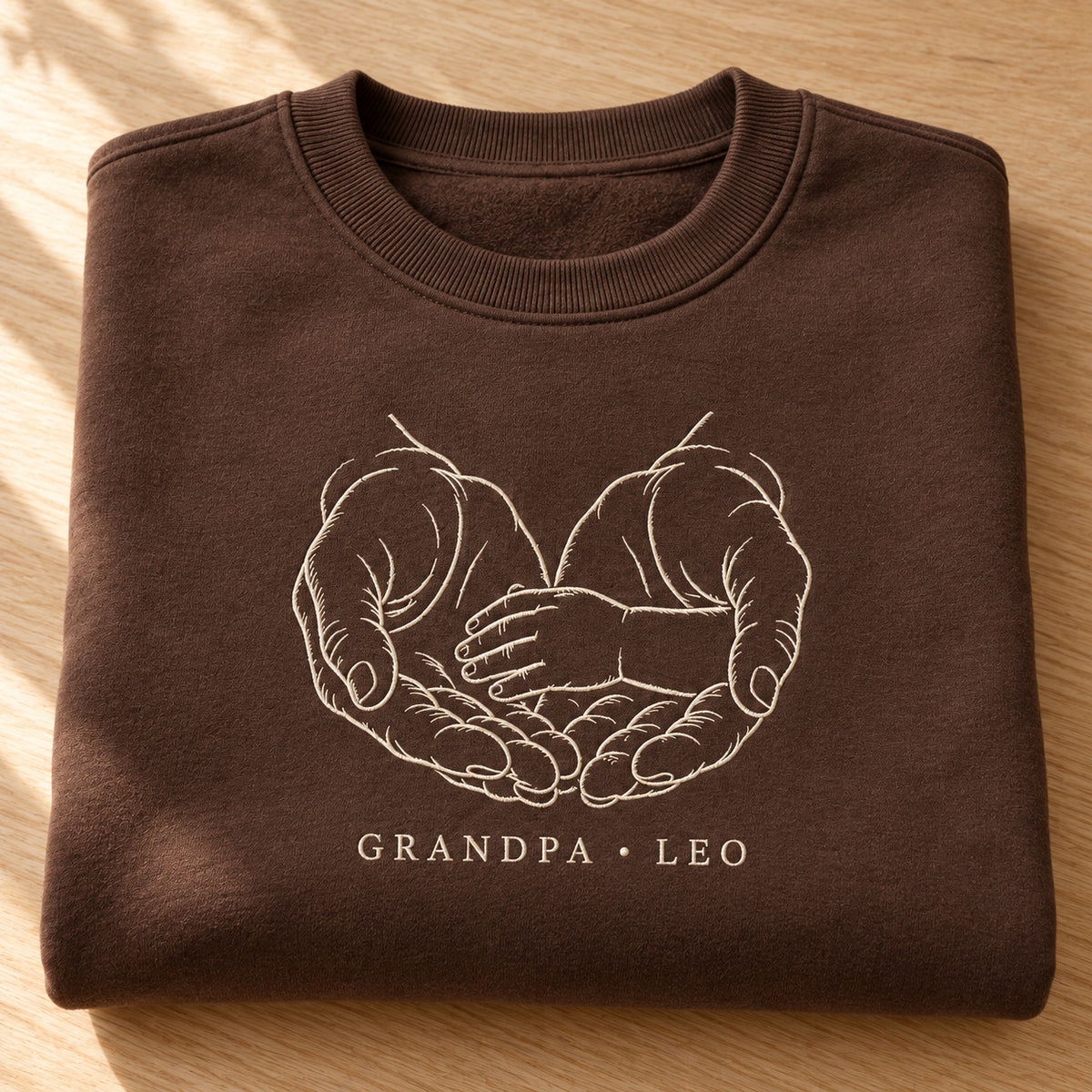 A Gentle Shelter personalized Grandpa hands design; Chocolate sweatshirt mockup, personalization detail; sample text GRANDPA • LEO
