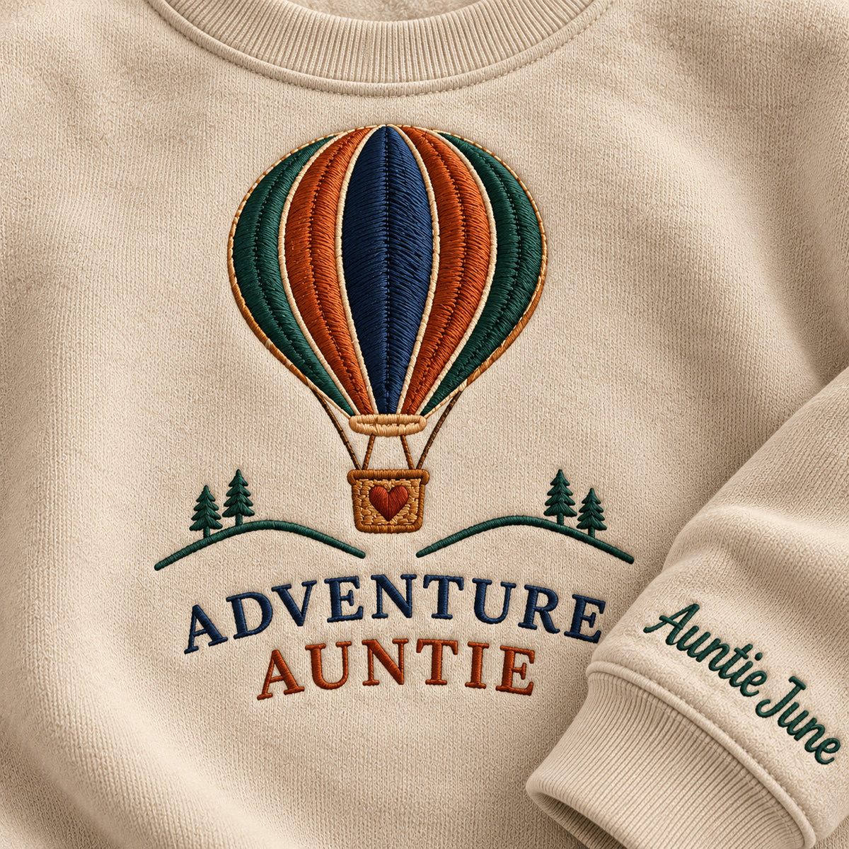Adventure Auntie sweatshirt concept mockup featuring a hot-air balloon above small trees and hills, sample personalization Auntie June, embroidery view