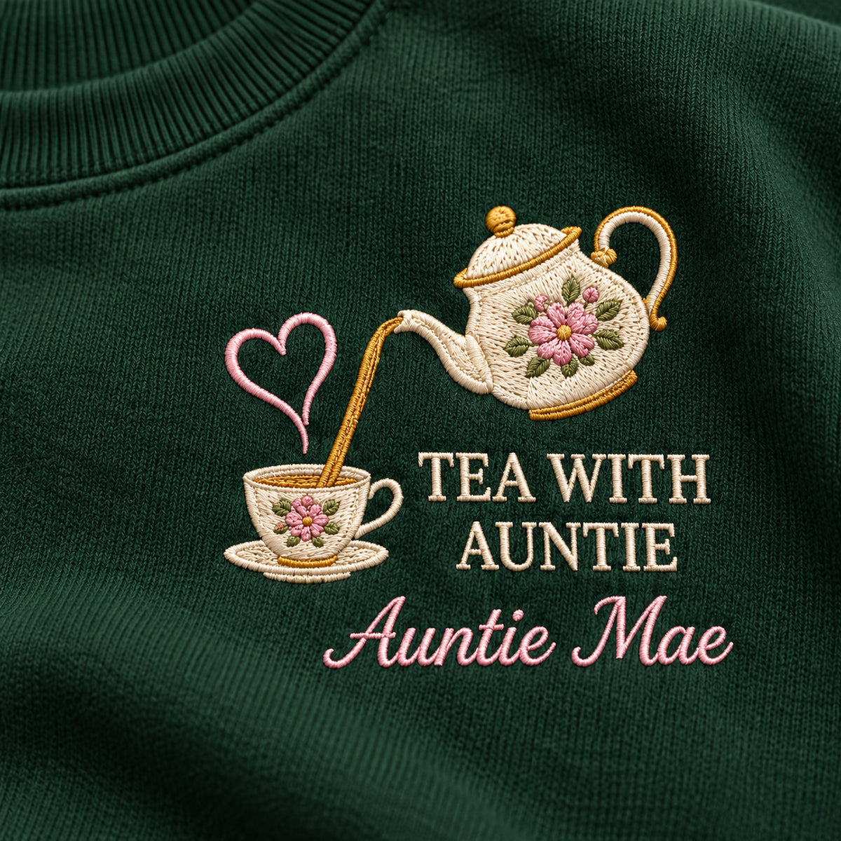 Tea with Auntie sweatshirt concept mockup featuring a floral teapot pouring into a teacup with a heart accent, sample personalization Auntie Mae, embroidery view