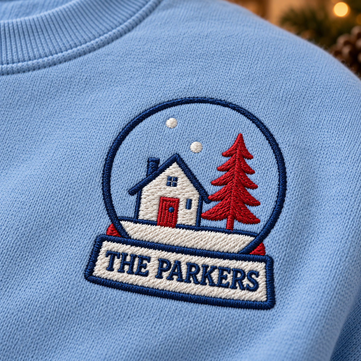 Home Snow Globe sweatshirt concept mockup featuring a house and tree inside a personalized snow globe, sample personalization PARKERS, embroidery view