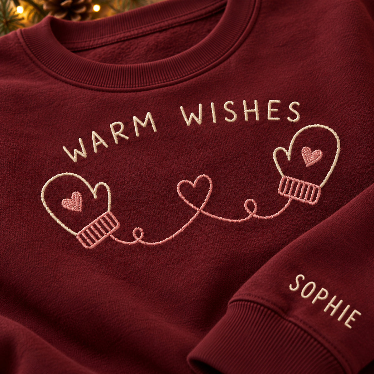 Warm Wishes Mittens sweatshirt concept mockup featuring two mittens connected by a heart-shaped cord, sample personalization SOPHIE, embroidery view