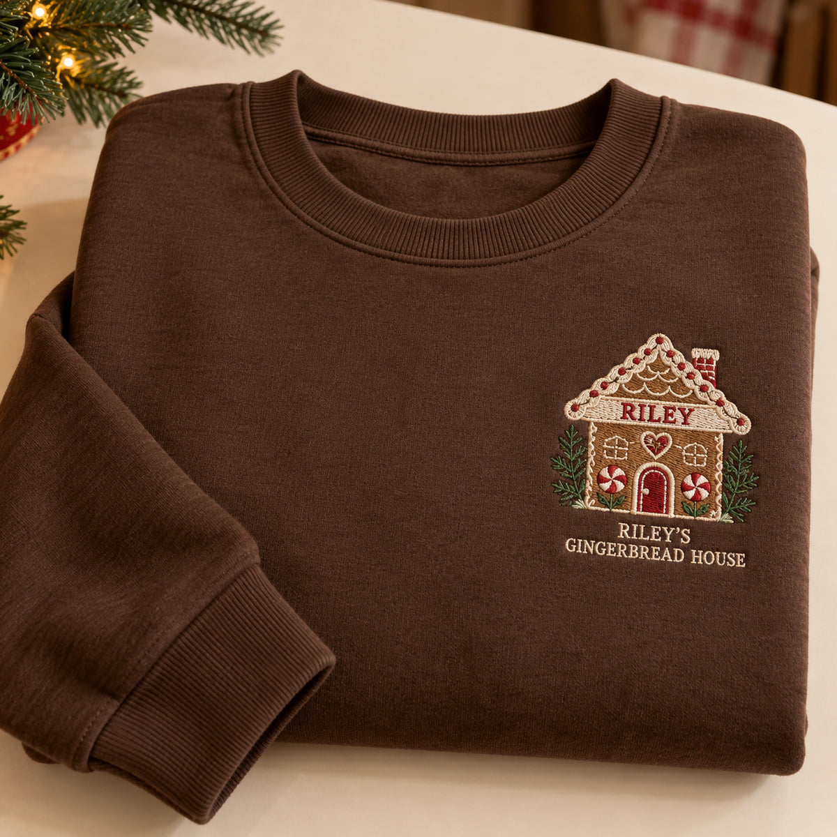 Gingerbread House sweatshirt concept mockup featuring a personalized gingerbread house with candy details, sample personalization RILEY, hero view