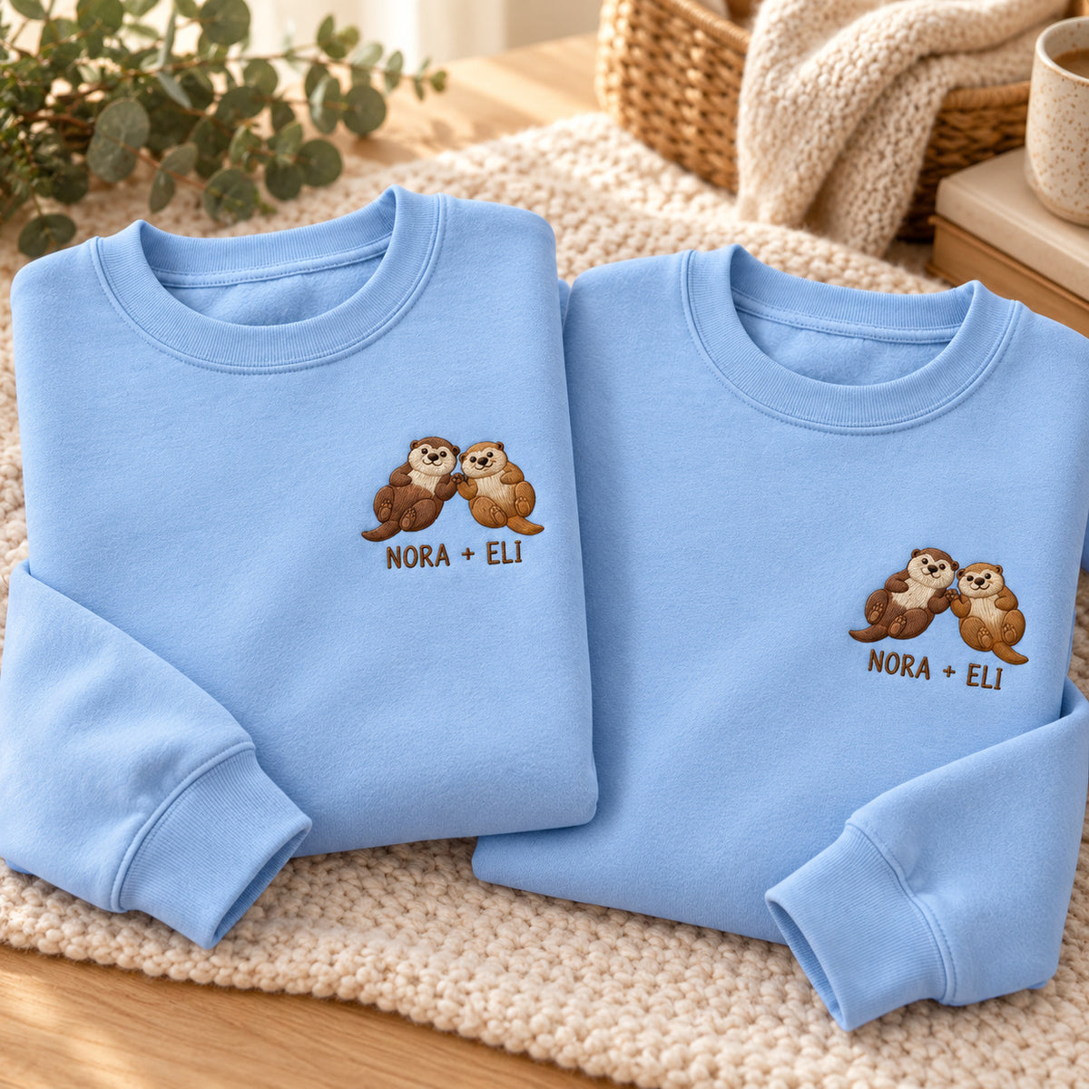 Holding Hands Otters sweatshirt concept mockup featuring two otters holding paws, sample personalization NORA + ELI, personalization view