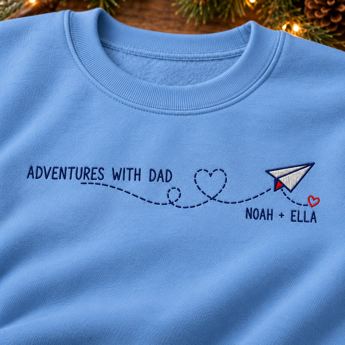 Adventures with Dad sweatshirt concept mockup featuring a paper airplane with a heart-shaped flight trail, sample personalization NOAH + ELLA, embroidery view