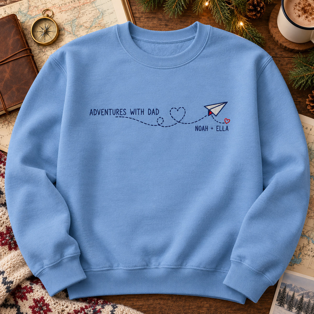 Adventures with Dad sweatshirt concept mockup featuring a paper airplane with a heart-shaped flight trail, sample personalization NOAH + ELLA, hero view