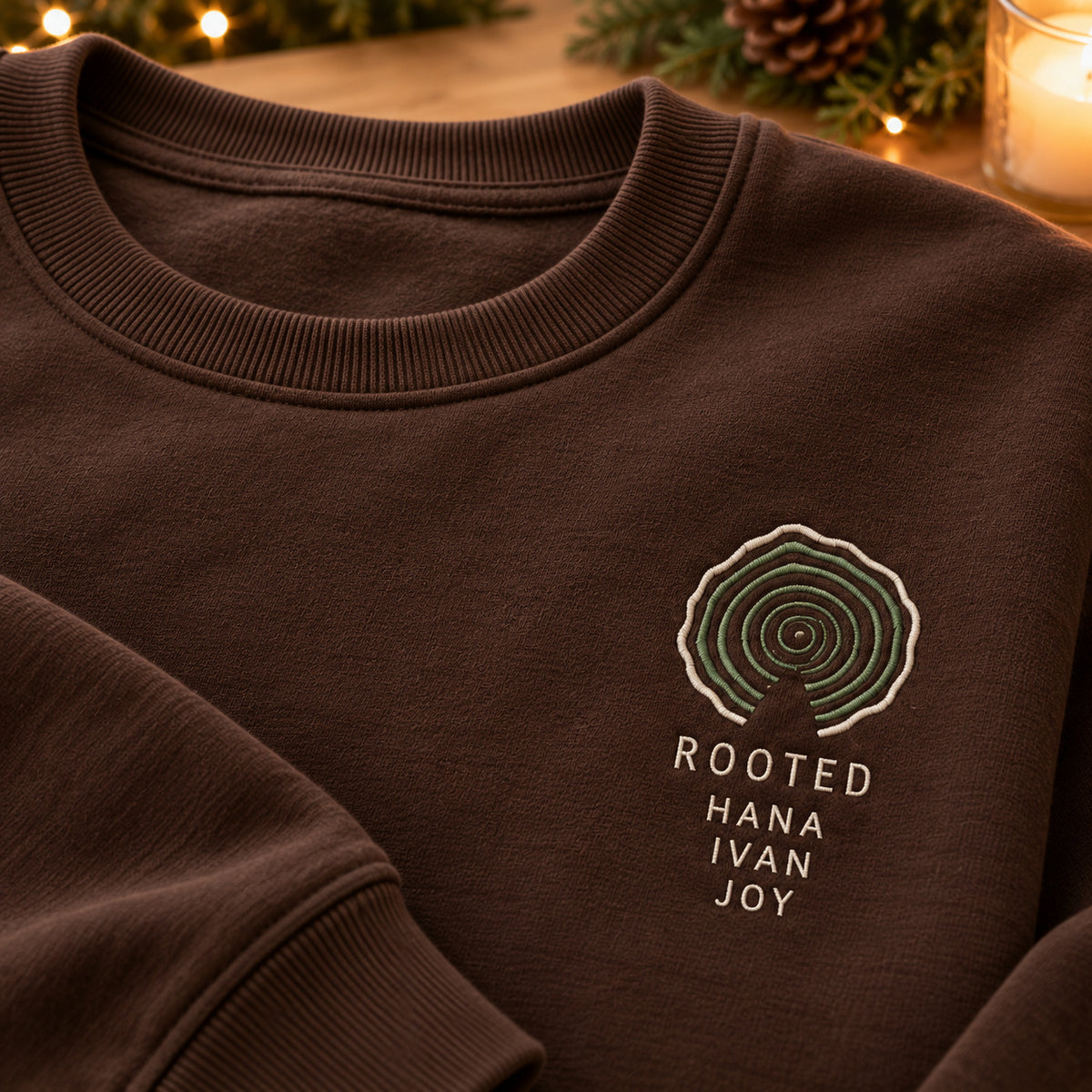 Rooted Family Tree Rings sweatshirt concept mockup featuring concentric tree rings above ROOTED lettering, sample personalization HANA / IVAN / JOY, embroidery view