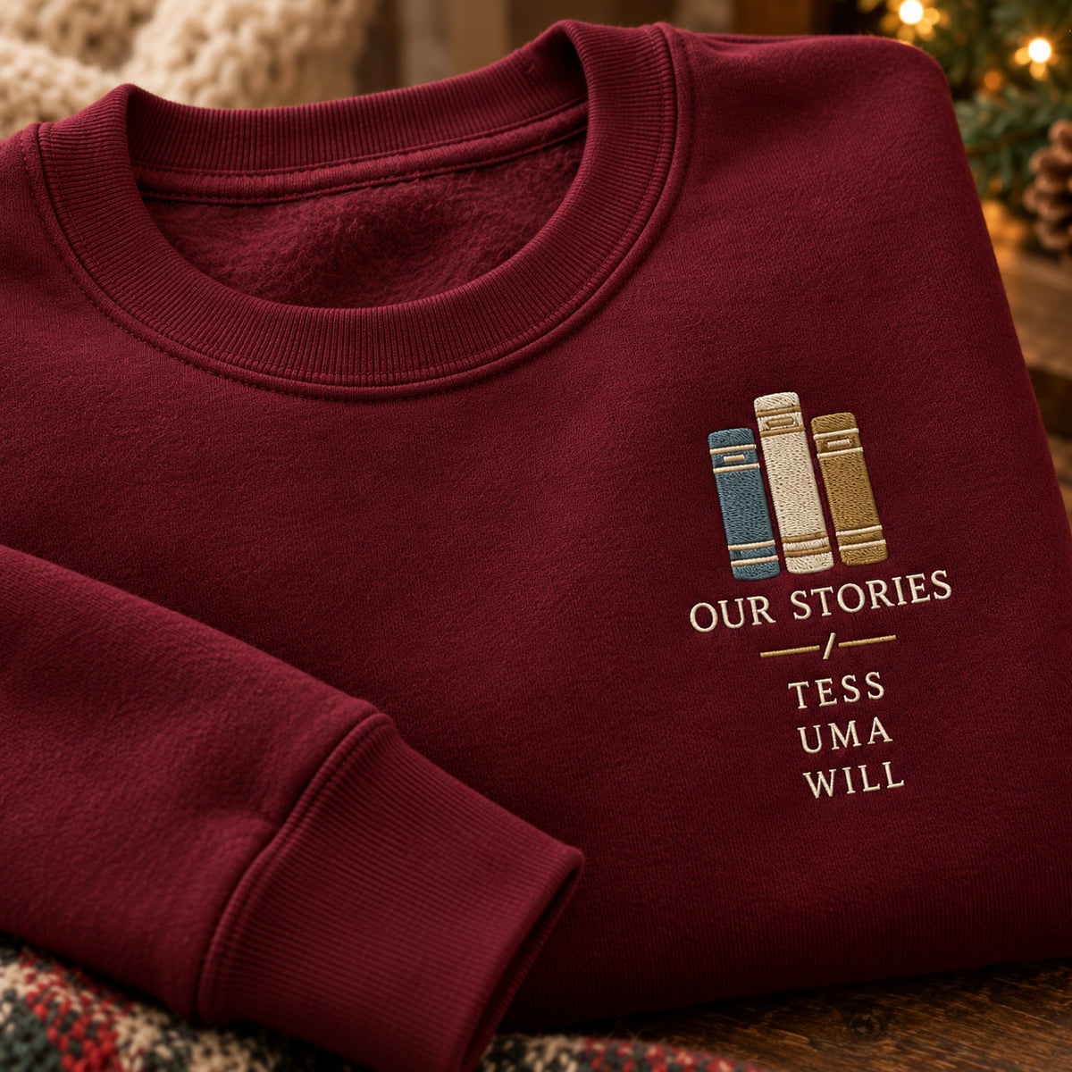 Our Stories Bookshelf sweatshirt concept mockup featuring three upright books above OUR STORIES lettering, sample personalization TESS / UMA / WILL, embroidery view