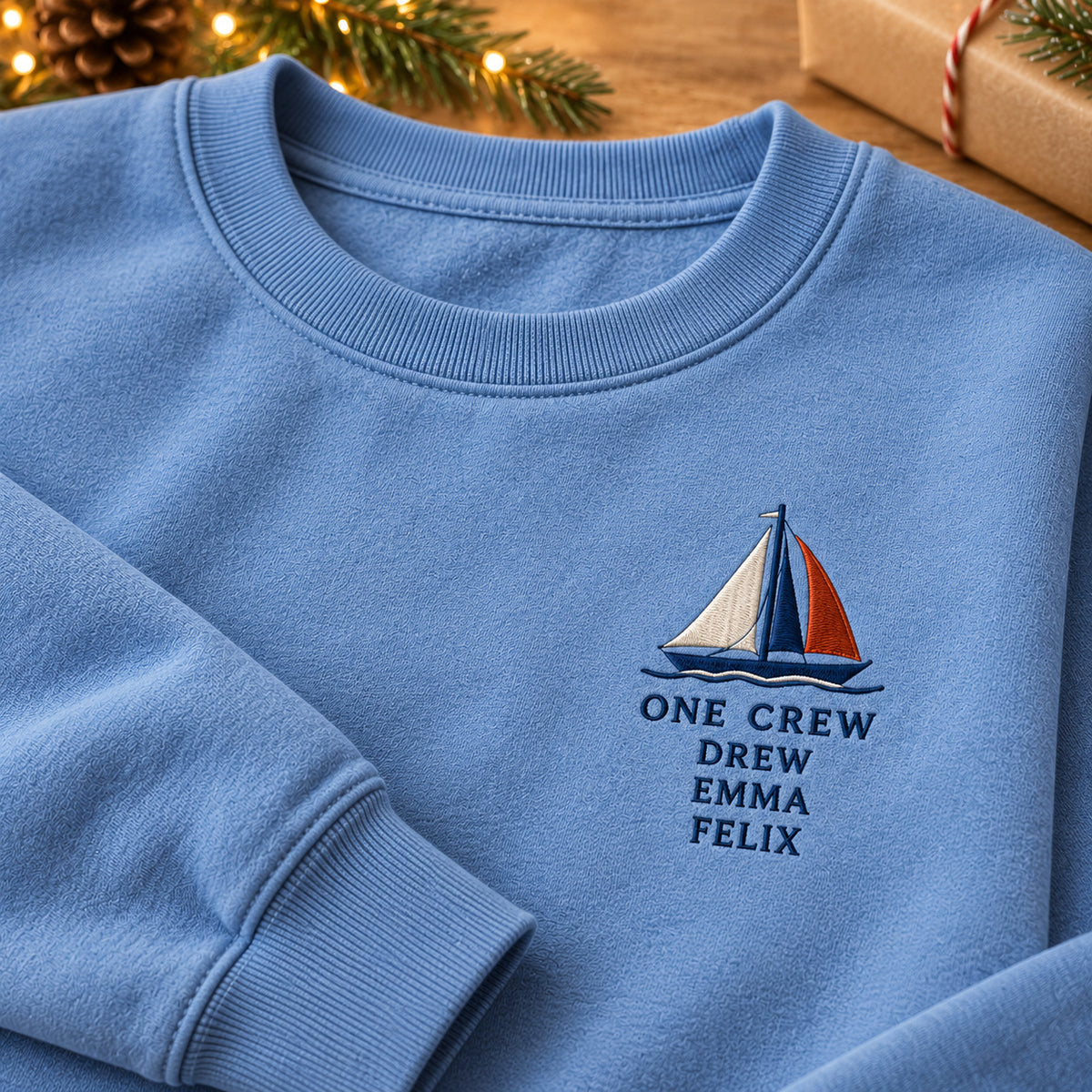 One Crew Sailboat sweatshirt concept mockup featuring a colorful sailboat above ONE CREW lettering, sample personalization DREW / EMMA / FELIX, embroidery view