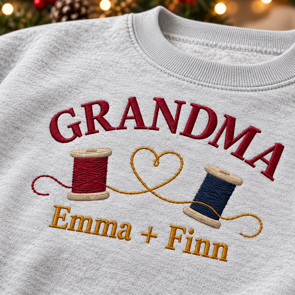 Grandma's Thread Spools sweatshirt concept mockup featuring two thread spools connected by a heart-shaped thread, sample personalization Emma + Finn, embroidery view
