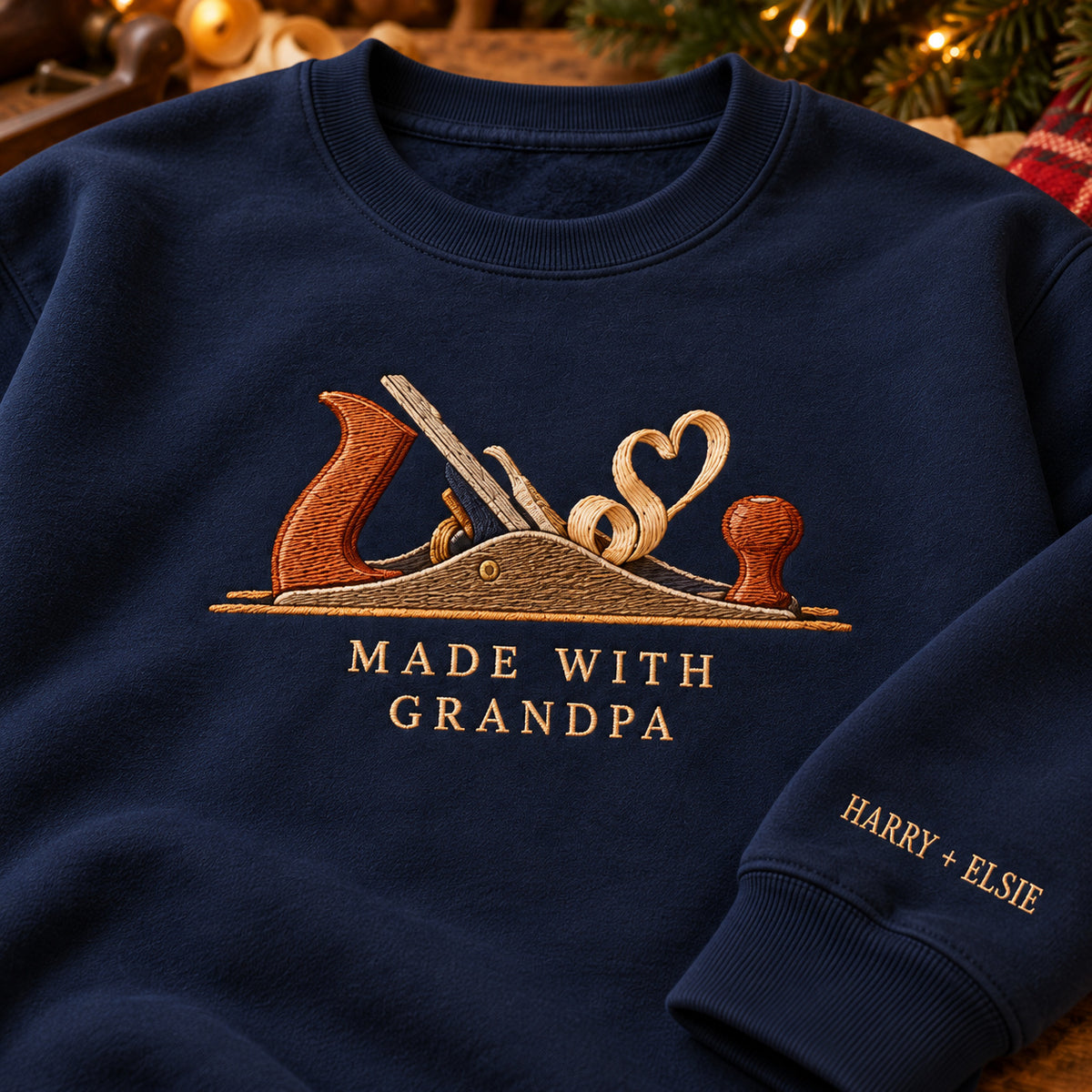 Made with Grandpa Woodwork sweatshirt concept mockup featuring a woodworking hand plane with curling wood shavings, sample personalization HARRY + ELSIE, embroidery view