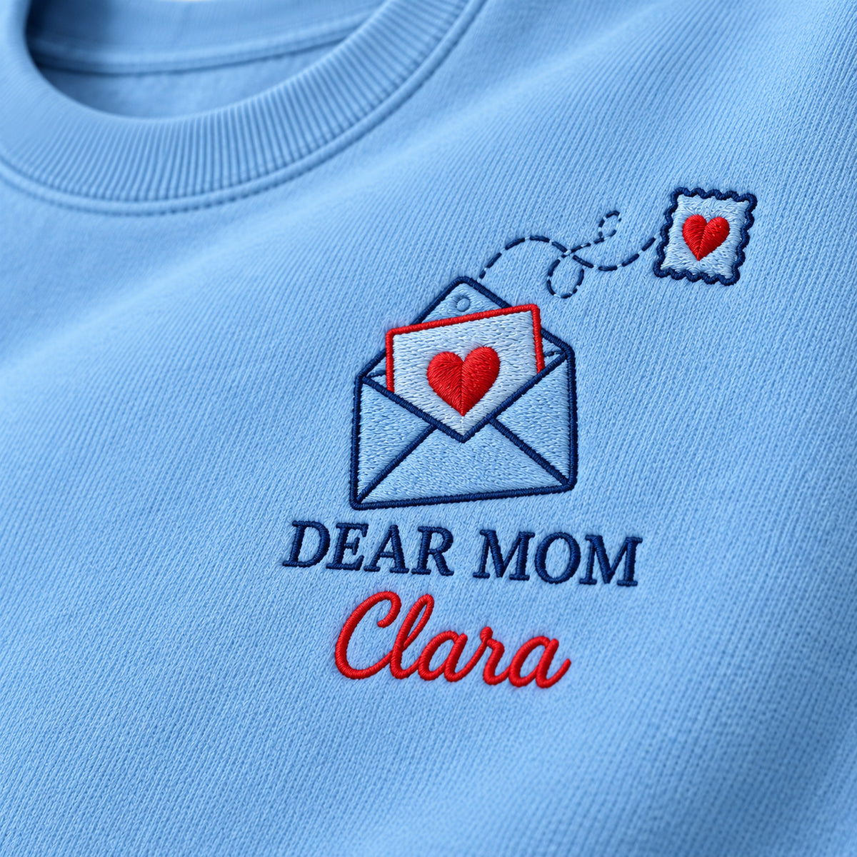 Dear Mom Letter sweatshirt concept mockup featuring an open envelope with a red heart letter and matching heart postage stamp, sample personalization Clara, embroidery view