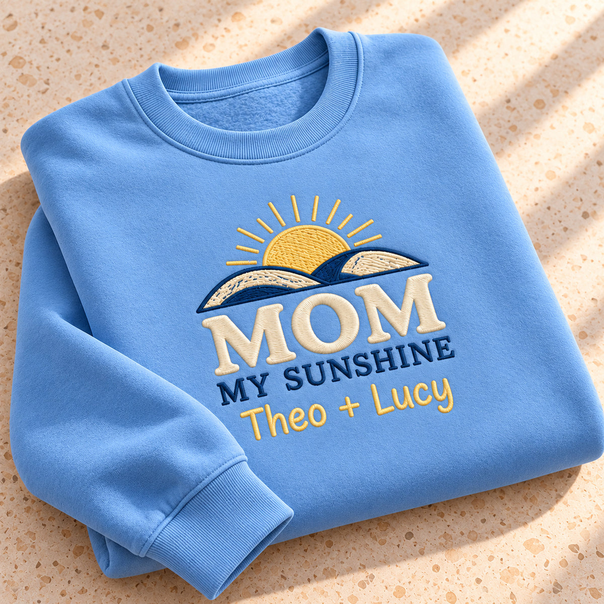 Mom's Sunshine sweatshirt concept mockup featuring a rising sun above curved hills, sample personalization Theo + Lucy, personalization view