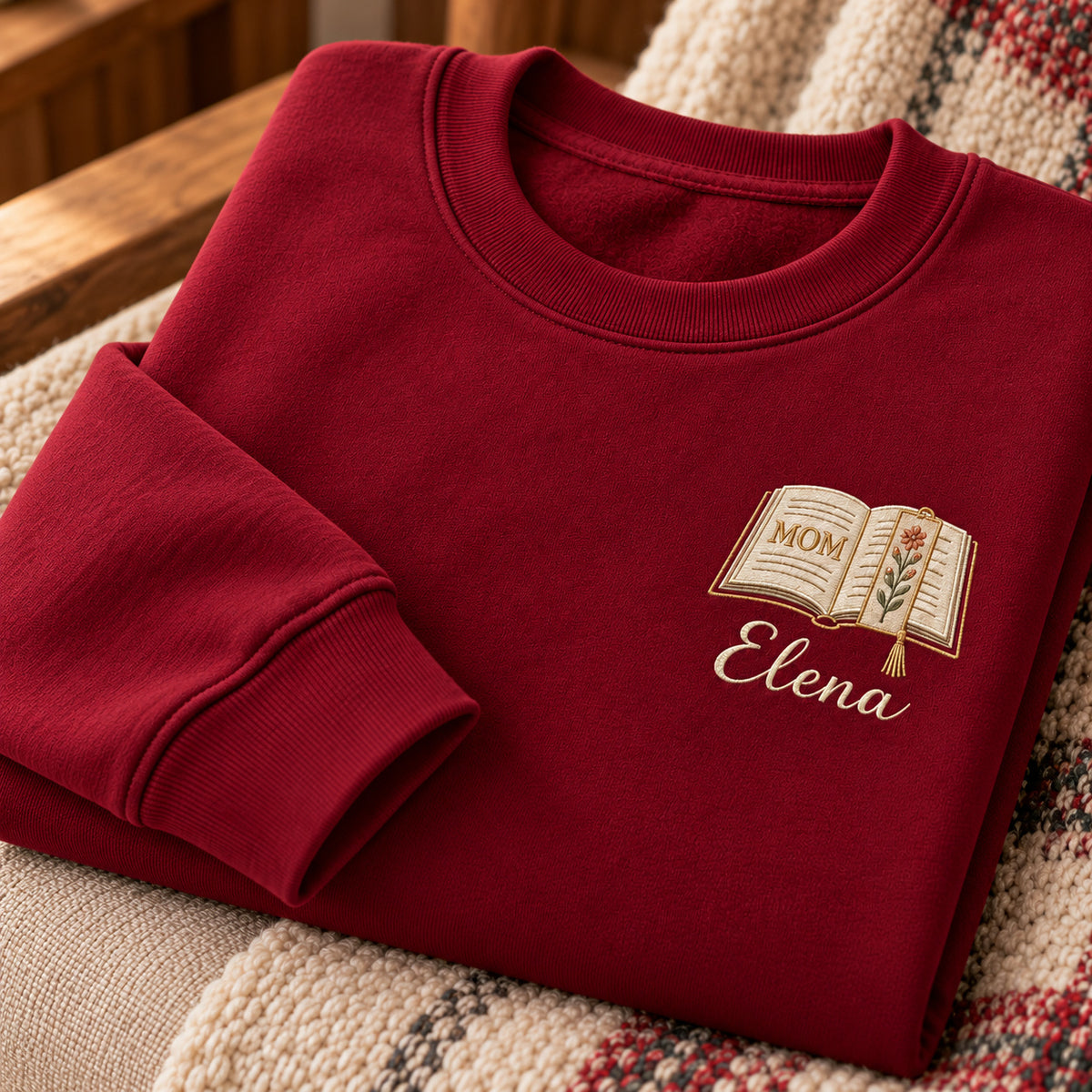 Motherhood Chapter sweatshirt concept mockup featuring an open book with a floral page and bookmark, sample personalization Elena, personalization view