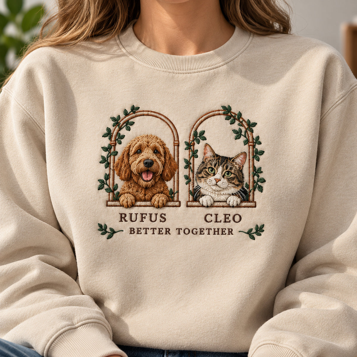 Two Little Windows sweatshirt concept mockup featuring a dog and cat in two leafy arched windows, sample personalization RUFUS     CLEO, embroidery view