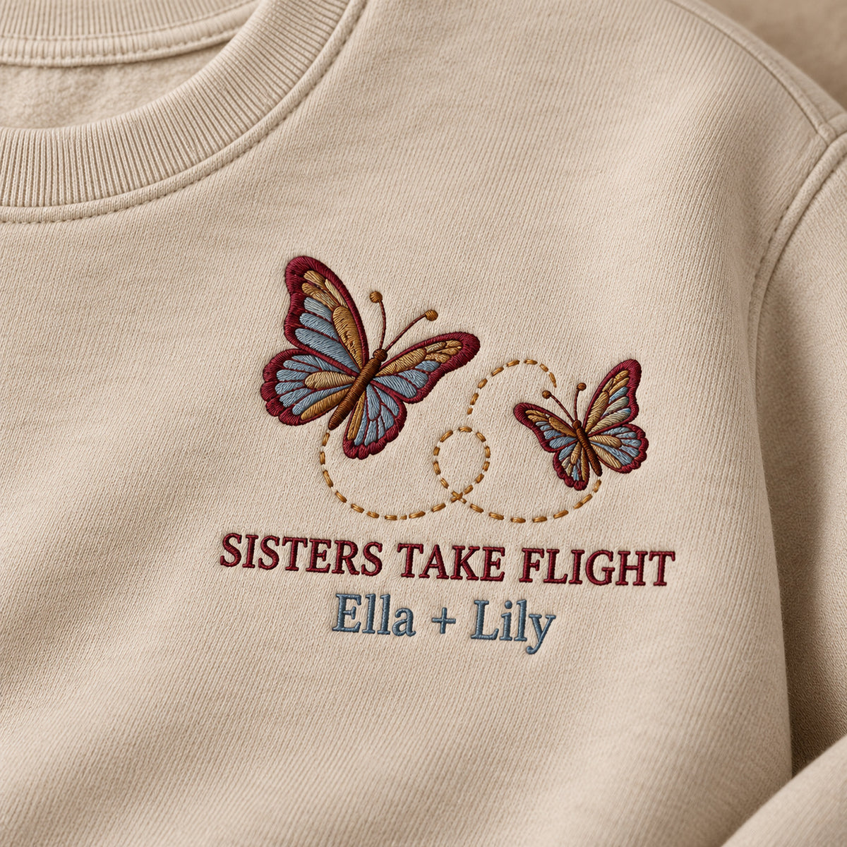 Sisters Take Flight sweatshirt concept mockup featuring two butterflies with a looping flight path, sample personalization Ella + Lily, embroidery view