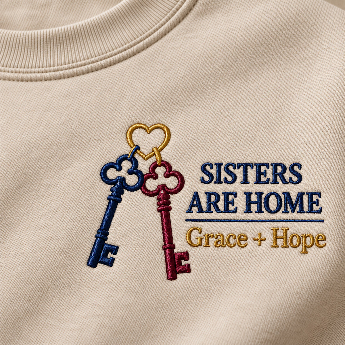 Sisters Are Home sweatshirt concept mockup featuring two keys joined on a heart-shaped ring, sample personalization Grace + Hope, embroidery view